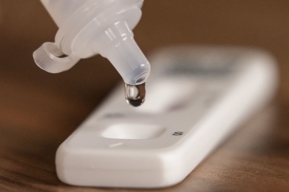 A gloved hand holding a dropper over a Covid-19 lateral flow test.