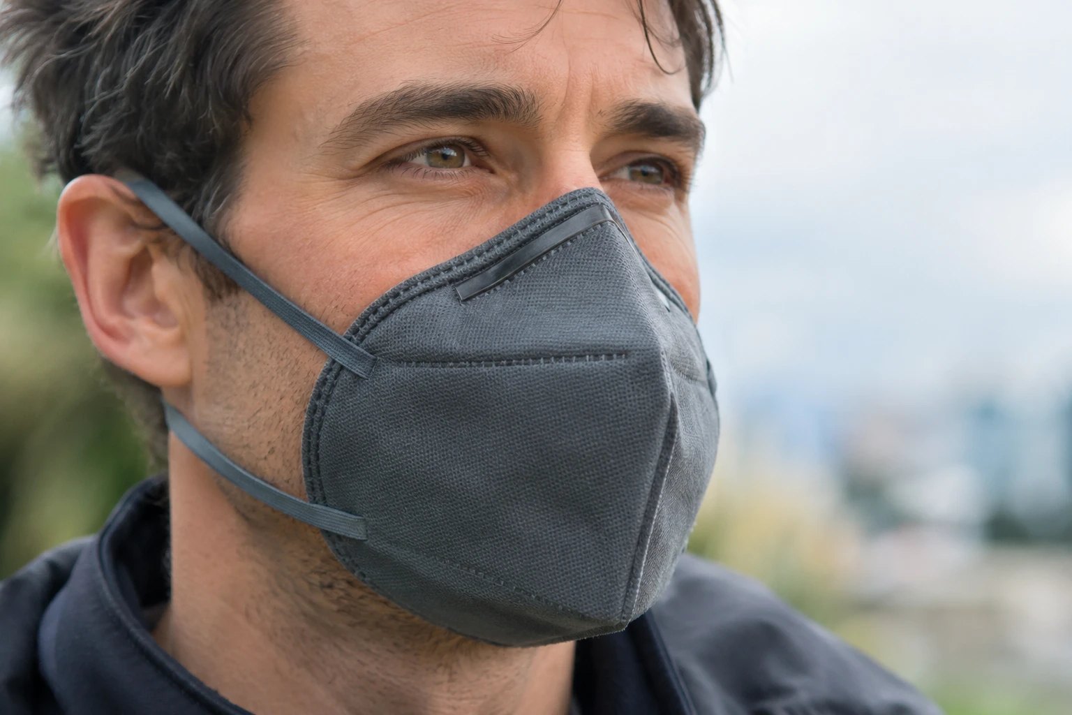A man wearing a grey FFP2 mask looks into the distance.