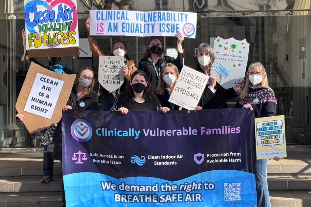 A group of campaigners wearing masks and holding placards and a banner.