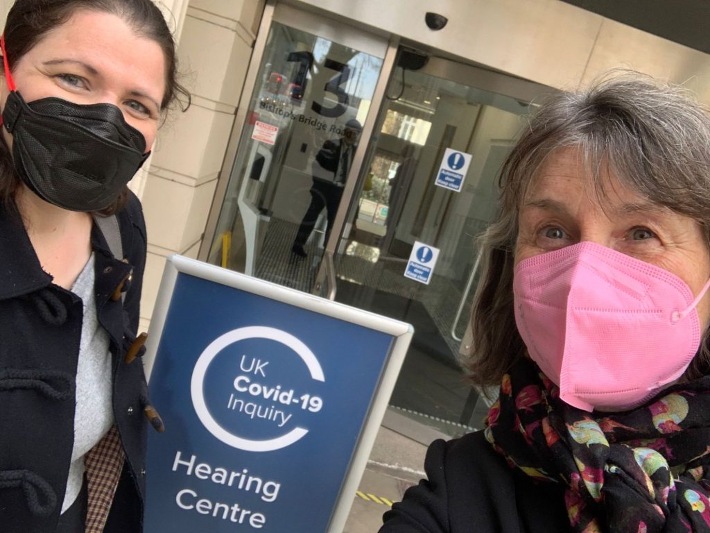 Lara Wong (left) and Dr Sharon Leighton, both wearing masks, take a selfie beside the UK Covid-19 Inquiry Hearing Centre sign at 13 Bishop’s Bridge Road, London.