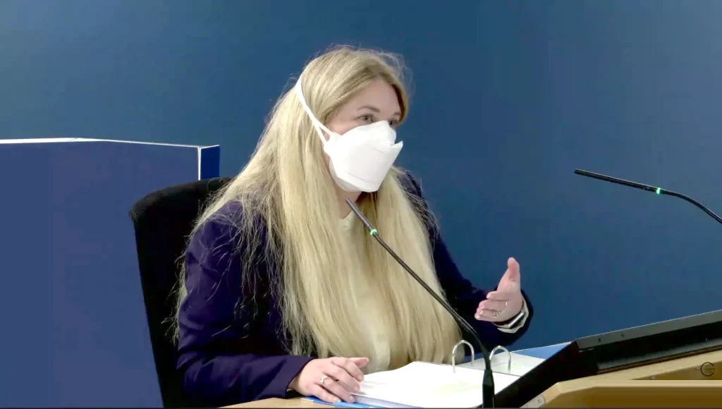 Dr Cathy Finnis, wearing a white FFP2 mask, gives evidence for Clinically Vulnerable Families at the UK Covid-19 Inquiry, gesturing as she speaks beside an open evidence binder.